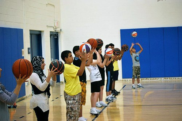 Jugendliche mit Basketballs auf einem Basketballfeld, im Hintergrund Türen und eine Wand.