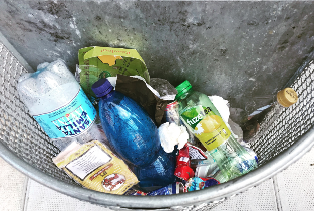 Ein Metallmüllcontainer voller verschiedener Plastikflaschen, Taschen und anderer Abfälle.