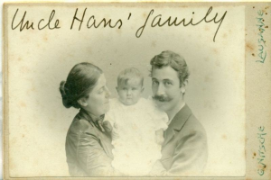 Ein altes Foto eines Mannes im Anzug und mit Krawatte, einer Frau mit einem Baby auf dem Arm und der Aufschrift "Onkel Hans' Familie" oben drauf, die alle warm und liebevoll aussehen.