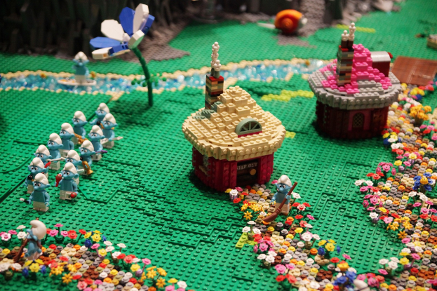 Ein Lego-Modell einer kleinen Stadt mit bunten Blumen, Spielzeugen, Häusern, Pflanzen und anderen Gegenständen vor einem leicht unscharfen Hintergrund.