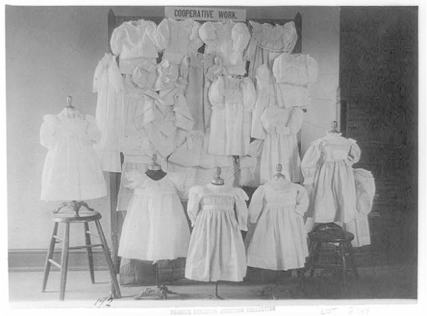 Ein Schwarz-Weiß-Foto eines Raums voller Kleider auf Puppen, mit einem Hocker links und einer Wand im Hintergrund. Unten im Bild steht der Text "frances berlin johnston collection".