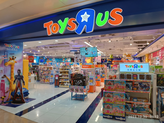 Ein Toys R Us-Laden in einem Einkaufszentrum mit Regalen voller Spielzeug, einem Schild mit Text, Deckenbeleuchtung und einem Wasserzeichen in der rechten unteren Ecke.