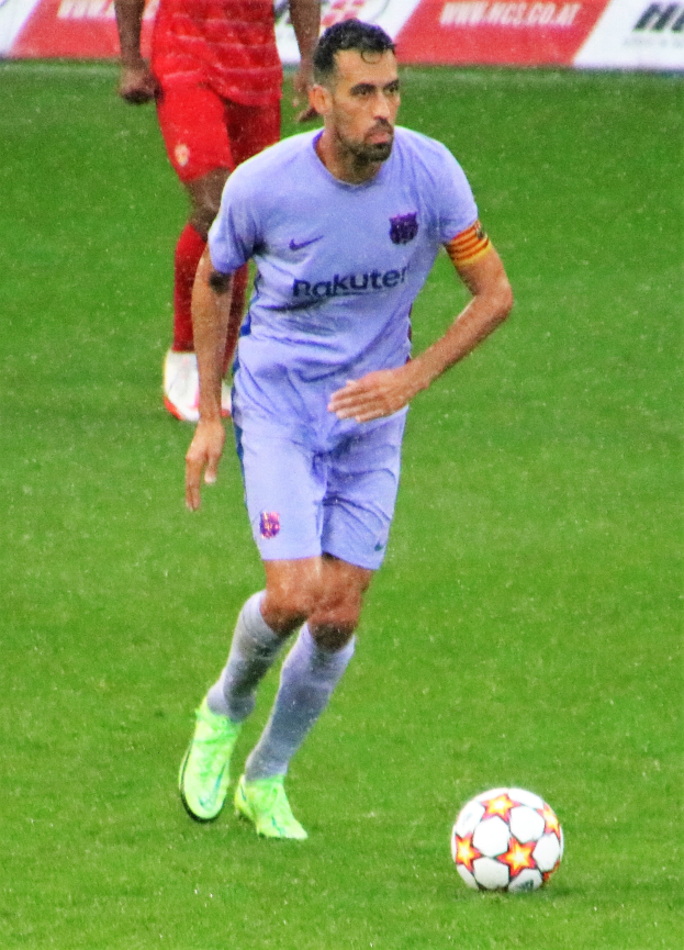 Ein Fußballspieler in einem Sportdress und -schuhen ist im Einsatz auf dem Feld, mit einer Texttafel im Hintergrund.