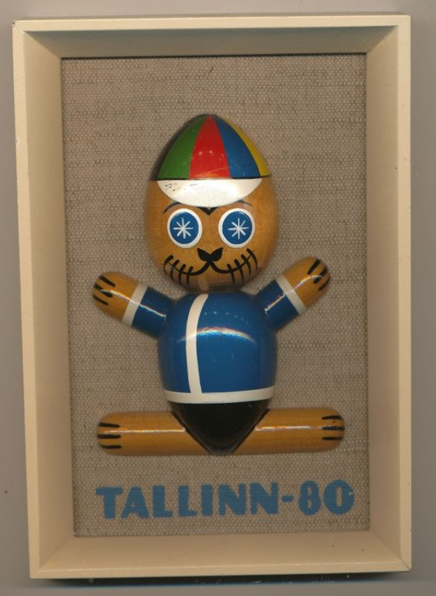 Holzspielzeug mit der Aufschrift "Tallinn-80" in einem weißen Rahmen mit einer blauen und roten Mütze.