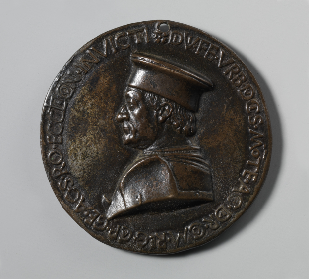 Eine bronzene Medaille mit einem ernsten Porträt eines Mannes in Hut, mit eingravierter Schrift.