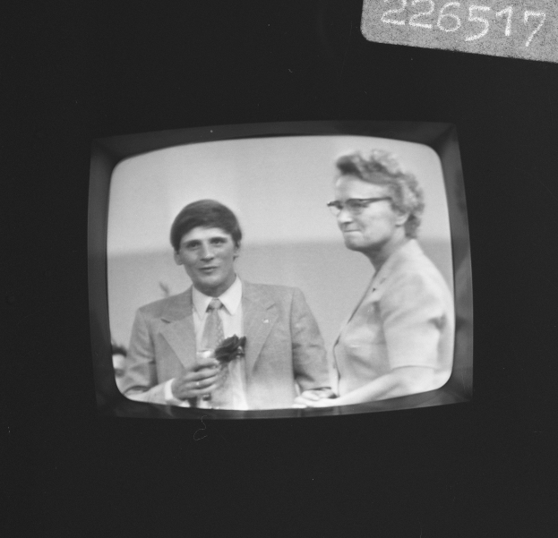 Ein Schwarz-Weiß-Foto eines Mannes im Anzug und einer Frau mit Brille auf einem Fernsehbildschirm.