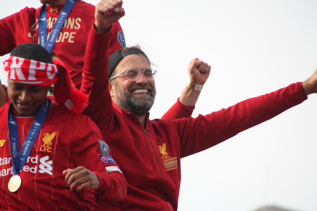 Liverpool-Trainer Jurgen Klopp, mit roter Jacke, feiert mit seinen Spielern nach dem Gewinn der UEFA Champions League, mit zwei medalien tragenden Personen in der Nähe und dem Himmel im Hintergrund.