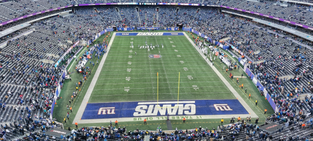 Ein voller Fußballstadion mit Spielern auf dem Feld, Torstangen und Texttafeln, von oben betrachtet.