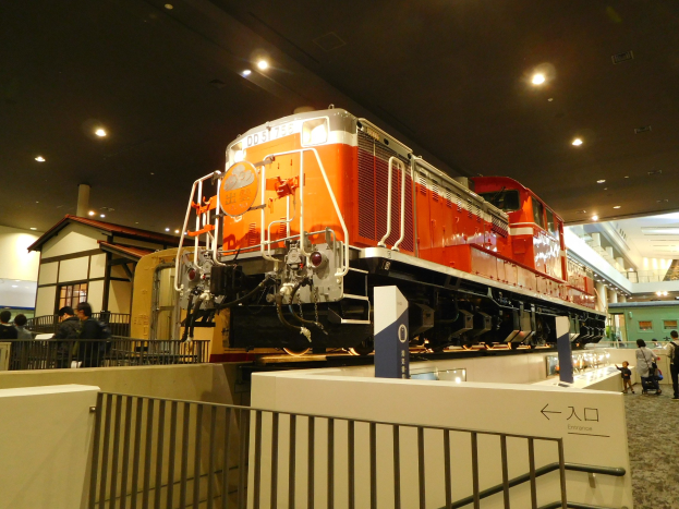 Roter und weißer Zug in einem Museum ausgestellt mit Besuchern, Informationsschild und Innenbeleuchtung.