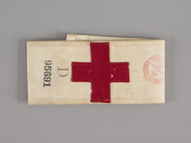 Ein rotes Kreuz-Erste-Hilfe-Set mit einem Text- und Stempel-versehenen Stoffbeutel, der auf einer Oberfläche liegt.
