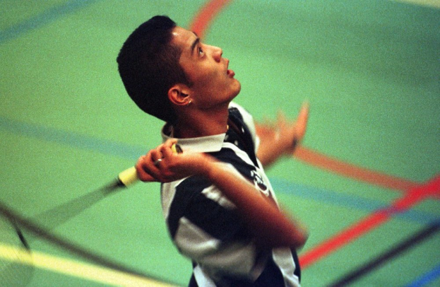 Ein junger Mann spielt Badminton auf einem Court und hält einen Schläger mit entschlossener Miene.