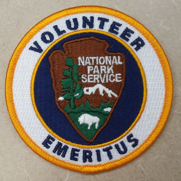 Runder Patch mit blauem Rand und weißem Hintergrund, der schwarzen Text "Volunteer National Park Service Emeritus" in einem gelben Kreis zeigt.