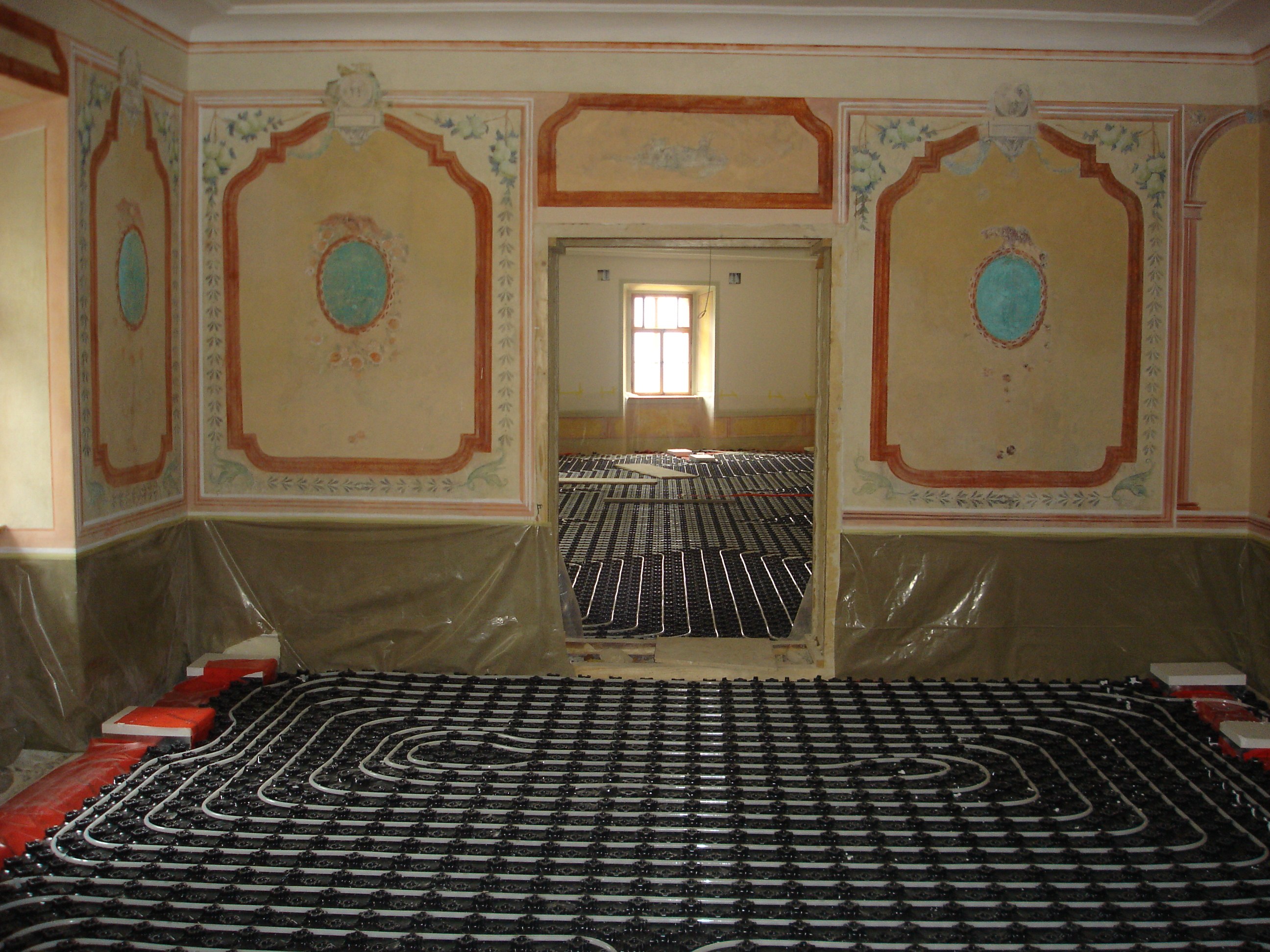 Ein Raum mit einer Fußbodenheizung in der Mitte, umgeben von Wänden und einem Fenster, mit verschiedenen Gegenständen in der Nähe auf dem Boden.