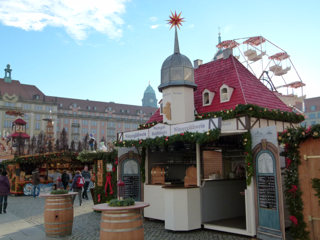 Ein belebter Weihnachtsmarkt in Nürnberg, Deutschland mit Menschen um geschmückte Stände, festliche Lichter, ein Riesenrad im Hintergrund und eine Tafel mit Text auf der rechten Seite.