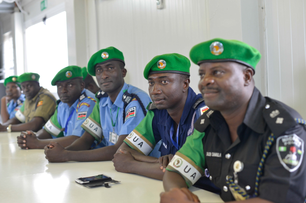 Gruppe von Polizeibeamten, die an einem Tisch mit Mobiltelefonen und anderen Gegenständen während einer Schulung in einem Raum mit Fenstern und Deckenleuchten sitzen.