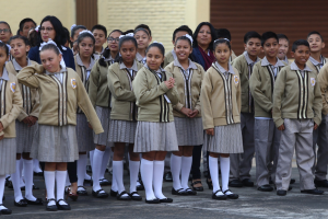 Eine Gruppe von Kindern in Schuluniformen vor einem Gebäude mit einer Wand und einem Rollladen im Hintergrund.