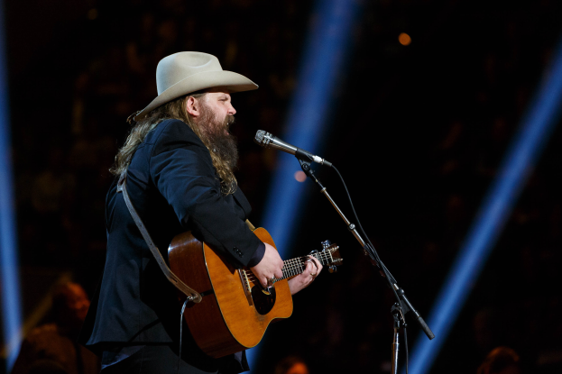 Chris Stapleton mit Hut, Gitarre spielend und ins Mikrofon singend während eines Auftritts auf dem CMA Music Festival in Nashville, Tennessee, mit ein paar Menschen im Hintergrund.