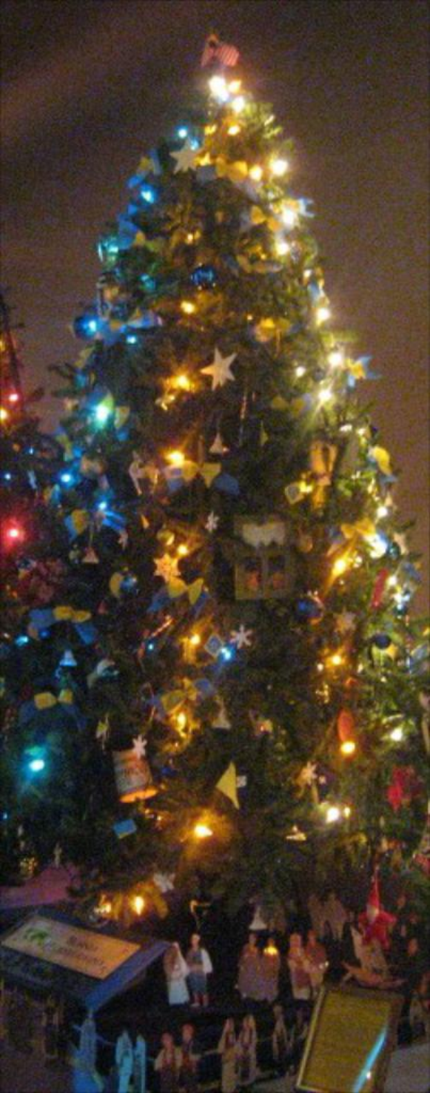 Ein geschm├╝ckter Weihnachtsbaum mit Menschenfiguren, die auf einem Tisch darunter platziert sind.