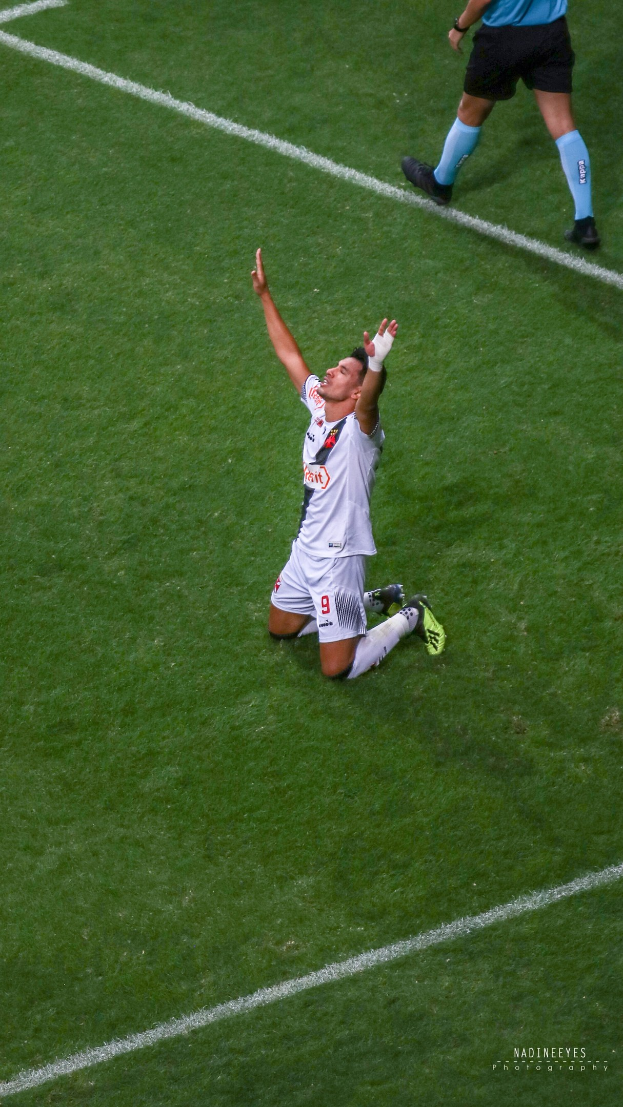 Ein Fußballer kniet auf dem Boden und streckt die Arme aus, um zu feiern, trägt eine Sportuniform und Fußballschuhe.