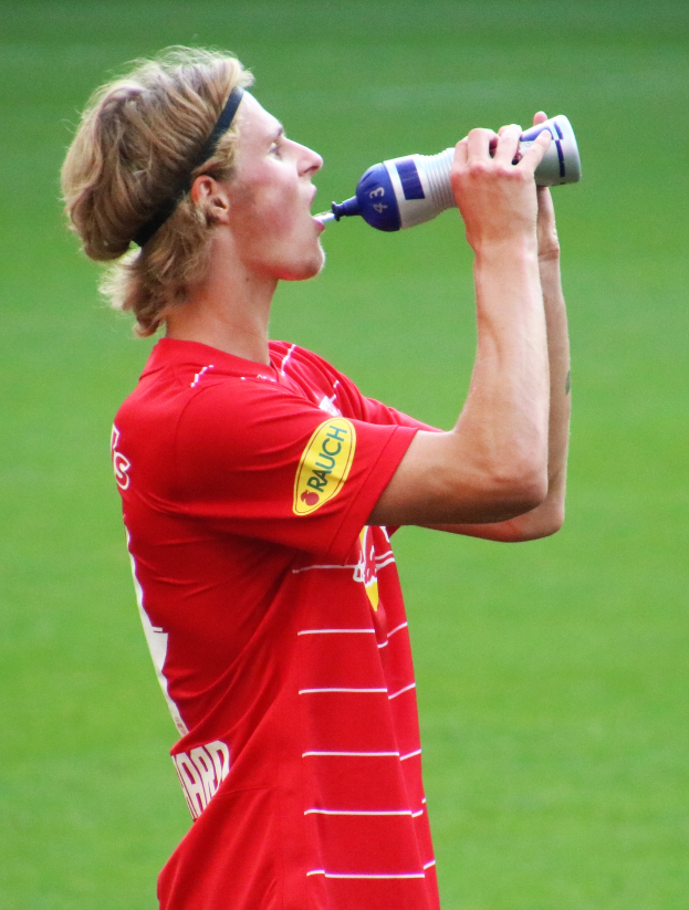 Mann in rotem T-Shirt trinkt aus einer Flasche auf einem Fussballfeld