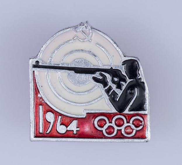 Ein Abzeichen mit einem Mann in rot-weiß gestreiftem Hemd und schwarzem Hut, der ein Gewehr auf ein Ziel richtet, mit der Aufschrift "1964 Olympische Spiele" und einem hellblauen Himmel mit weißen Wolken im Hintergrund.