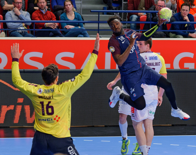 Eine Gruppe von Männern, die Handball spielen, auf einem Court mit einem Ball in der Luft, in einer Stadionatmosphäre mit Zuschauern und einem Scoreboard, das "Futsal-Weltmeisterschaft 2019 - Paris Saint-Germain vs. Bordeaux" anzeigt.