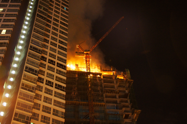 Zwei Gebäude, eines mit sichtbaren Flammen, unter einem klaren Himmel.