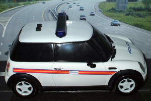 Weißes Polizeiauto vor fahrendem Verkehr auf einer grünen und baumbestandenen Straße vor der Stadt.