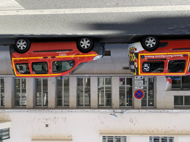 Zwei Rettungswagen nebeneinander in einer Tiefgarage geparkt mit einem Gebäude im Hintergrund, das Glasfenster und Schildertafeln aufweist, und einer Überwachungskamera an der Wand unten.