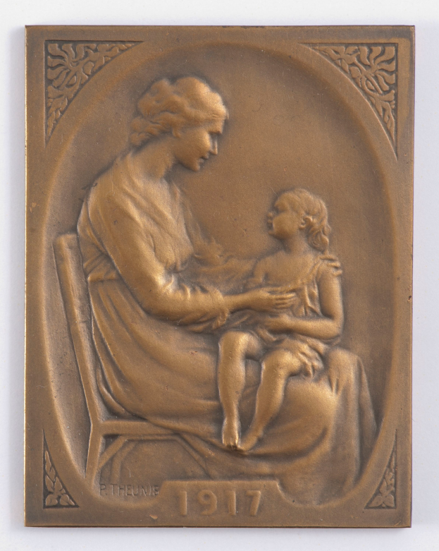 Eine Bronzetafel, die eine Frau mit sanftem Gesichtsausdruck zeigt, die auf einem Stuhl sitzt und ein zufriedenes Kind hält, mit der Inschrift "Mutter und Kind".