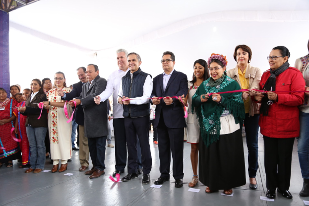 Eine Gruppe von Menschen bei einer Scherenschnittzeremonie, die strahlend eine Schere halten, mit Papieren auf dem Boden und einem weißen Tuch im Hintergrund.