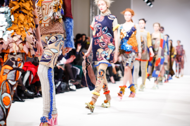Eine Gruppe von Frauen läuft über den Laufsteg bei der London Fashion Week, mit Zuschauern auf Stühlen und hellen Scheinwerfern im Hintergrund.