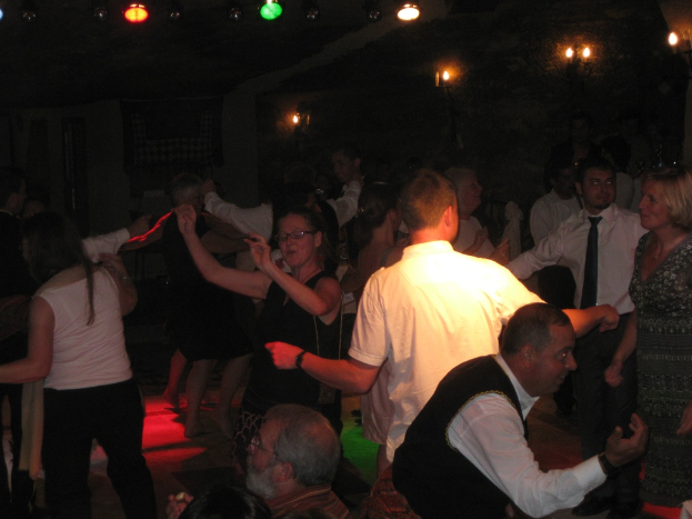 Eine lebendige Partyszene mit tanzenden Menschen auf der Tanzfläche unter verschiedenen bunten Lichtern in einem dunklen Raum.
