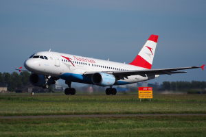 Airbus A320-200 der Austrian Airlines startet am Frankfurter Flughafen mit einer Tafel im Vordergrund, Gras, Bäumen, Gebäuden und einem klaren blauen Himmel im Hintergrund.