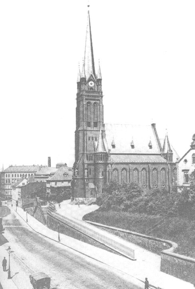 Schwarzes und weißes Foto einer Stadtstraße mit St. Peter's Church im Hintergrund in Wiesbaden, Deutschland, gesäumt von Gebäuden, Bäumen und Fahrzeugen sowie einigen Fußgängern.