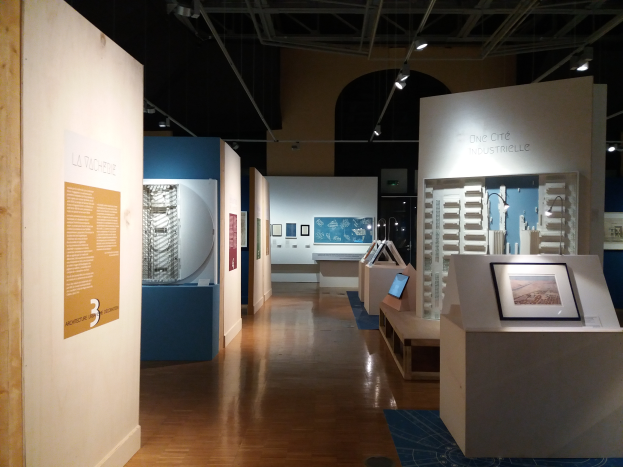 Ein Raum voller verschiedener Kunstwerke, darunter Foto Rahmen auf Tischen, Texttafeln an den Wänden, Deckenleuchten und ein Teppichboden, in der Ausstellung des Museums of Modern Art.