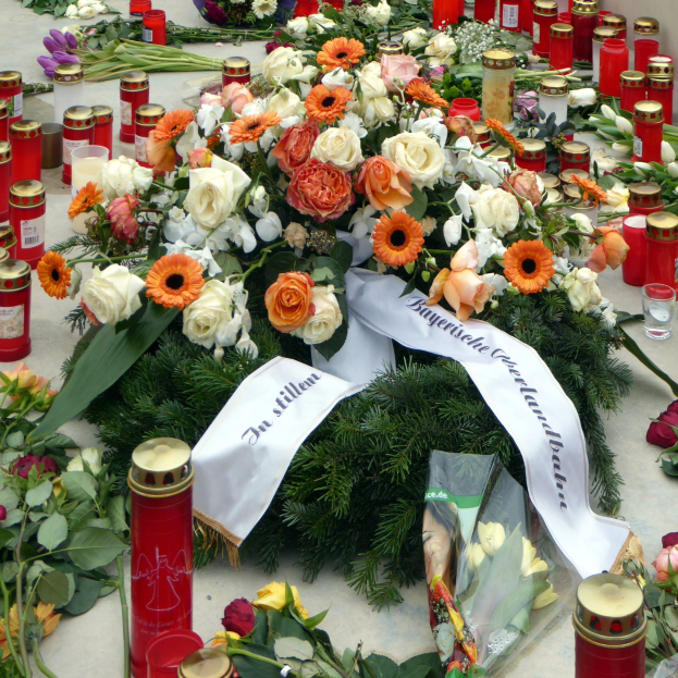 Mahnmal in Berlin mit Blumen und Kerzen vor einer Wand auf dem Boden