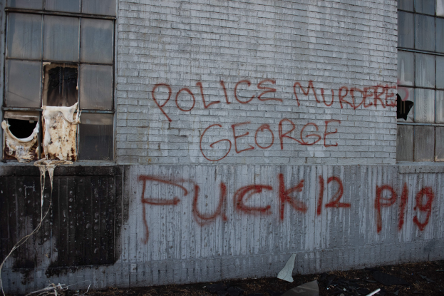 Ein Gebäude mit Graffiti, das "Polizeimord George Fuck 12 P19" auf der Seite trägt, mit Fenstern und verschiedenen Gegenständen vorne drauf.