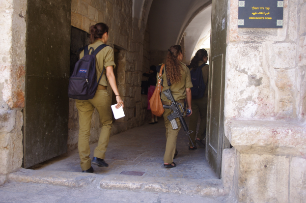 Israelische Soldaten in Uniform gehen durch einen Torbogen im Alten Stadt Jerusalem, einer hält eine Waffe und ein Blatt Papier, mit einer Schautafel auf der rechten Wand.