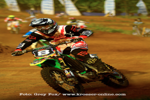 Mehrere Motorradfahrer mit Helmen rasen, mit Text am Bildrand.