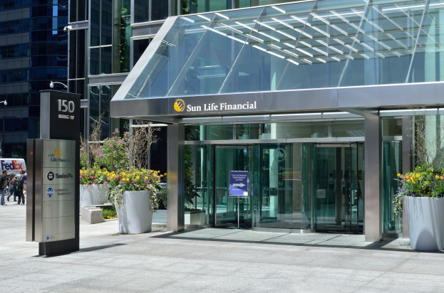 Moderner Glasturm der Sun Life Financial in Toronto mit einer Hinweistafel, Topfpflanzen mit Blumen, Menschen, Straßenmast, Hinweistafel, Fahrzeugen und einer bewölkten Himmel.