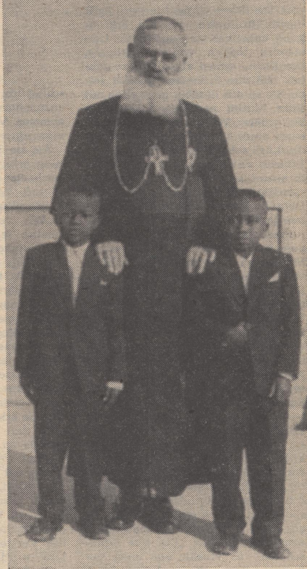 Ein Schwarz-Weiß-Foto eines Mannes, der neben zwei Jungen steht, alle tragen Blazer und Krawatten, mit Text unten, der darauf hindeutet, dass der Mann ihr Vater ist.