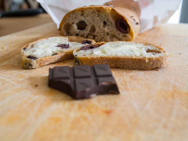 Eine Schokolade, Brotscheiben mit Creme und andere Artikel auf einer hölzernen Oberfläche mit einem weißen Hintergrund.