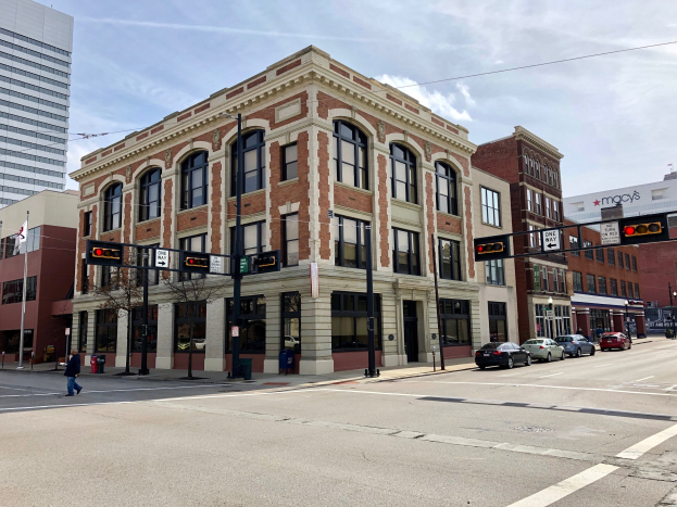 Großes Backsteingebäude an einer Straßenkreuzung, umgeben von städtischer Infrastruktur und Fußgängern.