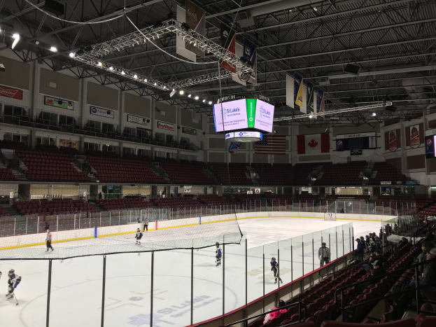 Ein Hockey-Spiel im St. Louis Blues Arena - Spieler auf dem Eis und Zuschauer auf beiden Seiten, unter einer Decke mit Lampen und Trägern, sowie Bannern mit Text und Fahnen an den Wänden.