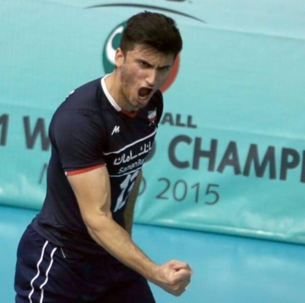 Mann in blauem Hemd und schwarzen Shorts beim Handballspielen mit einem "Kabaddi World Cup 2015"-Plakat im Hintergrund.