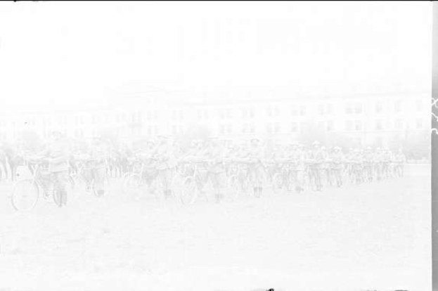 Schwarzes Foto von Radfahrern, die durch den Schnee fahren, mit einem Gebäude im Hintergrund.