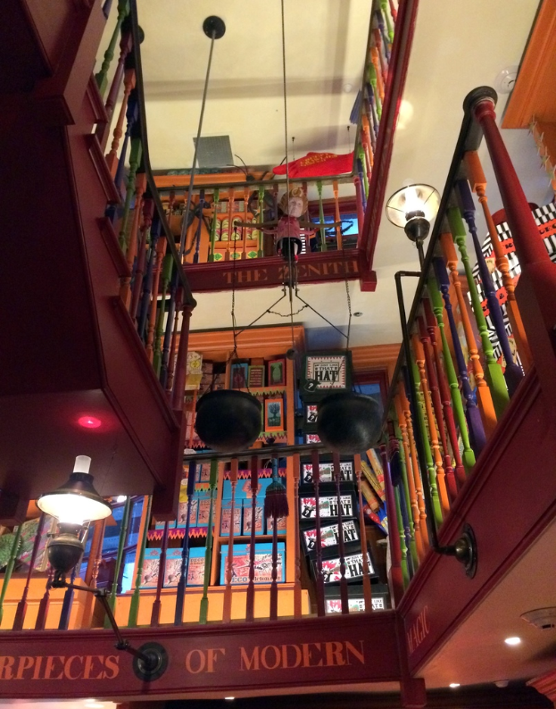 Ein Gebäude mit Treppe, Zaun, Laternen, einer Puppe, einem Schild und einem Dach.