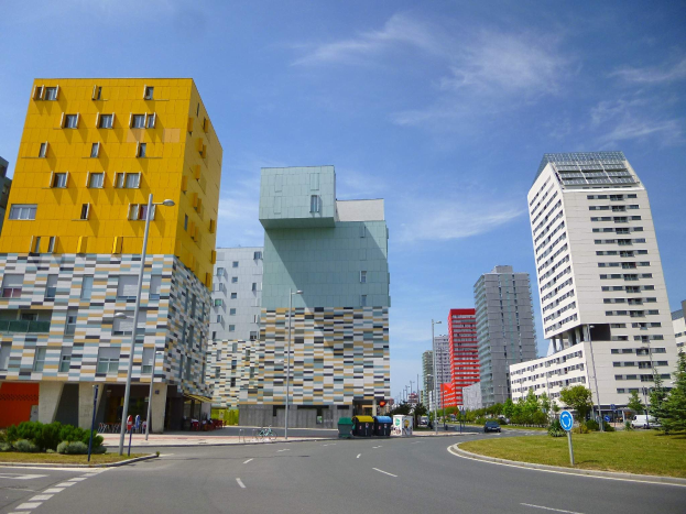 Eine Stadtstraße mit hohen Gebäuden im Hintergrund, Straßenlaternen, Autos, Informationsschildern, Büschen, Bäumen und einer bewölkten Himmel, mit Architektur der Universität Rotterdam.