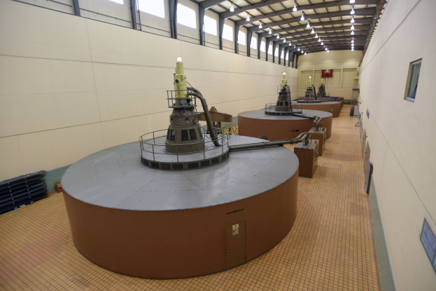 Großer Raum mit zahlreichen Metalltanks, Industriemaschinen, Wänden, Fenstern und Deckenlampen, wahrscheinlich Teil einer Kernreaktoranlage mit verstreuter Ausrüstung.